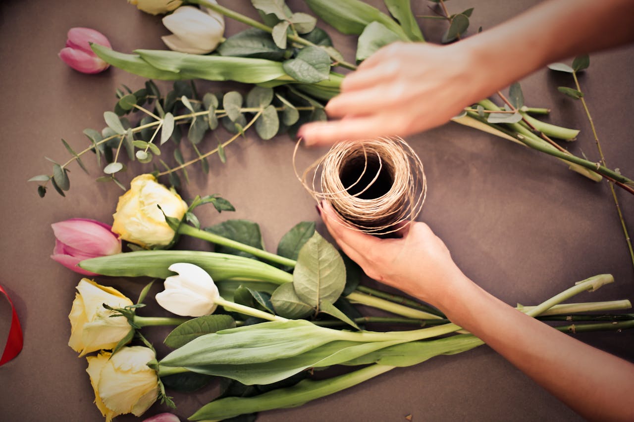 A woman arranging pink and yellow tulips with twine on a table, perfect for floral decor inspiration.