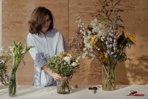 A florist arranges a vibrant flower bouquet in a wooden interior studio setting.