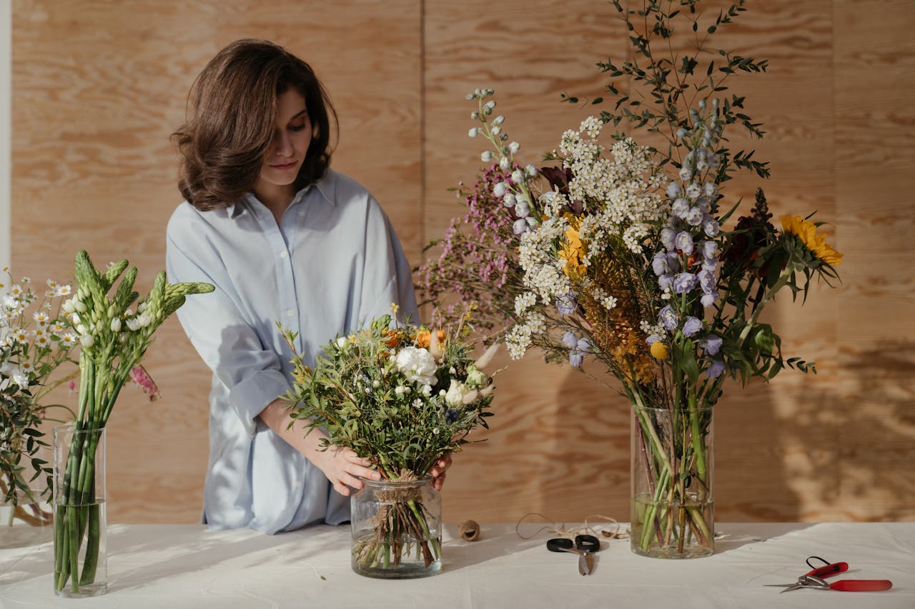 A florist arranges a vibrant flower bouquet in a wooden interior studio setting.