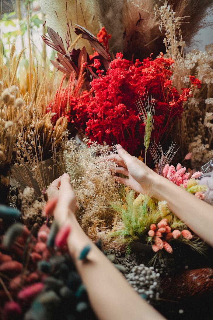 From above of crop anonymous female touching bouquet of dried flowers while decorating counter of floristry store
